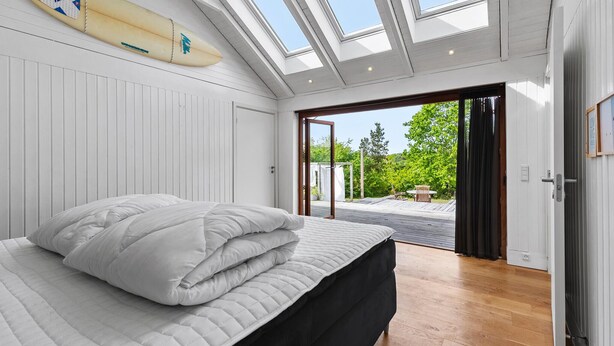 A bedroom with a bed, a surfboard, skylights, and a view of the outdoors. - Cozy home in Vejby with sauna (Vejby)