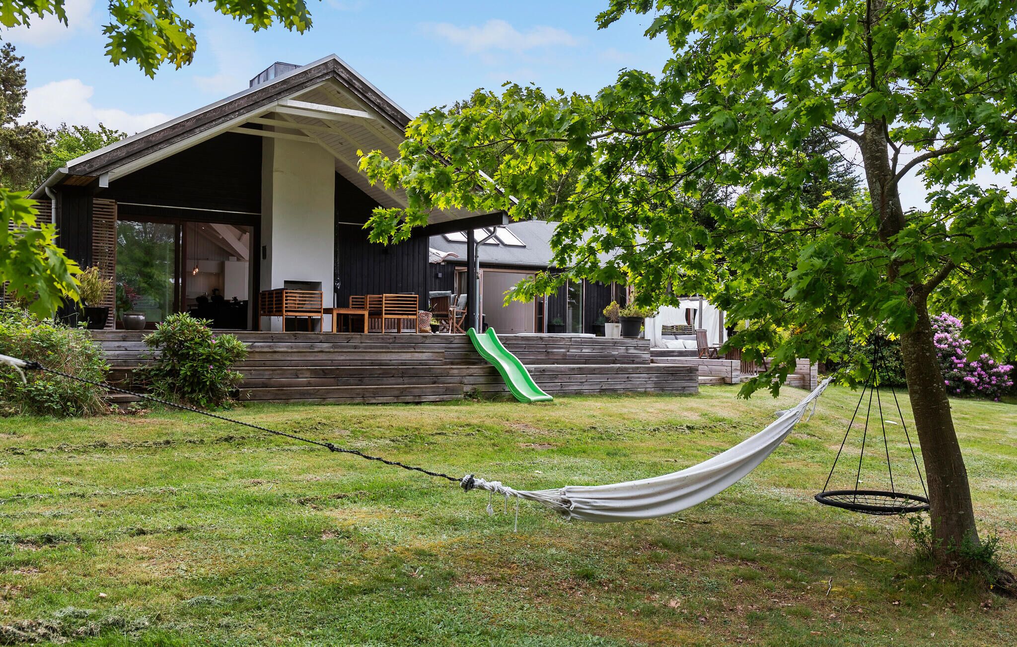 A house with a covered porch, a green slide, and a hammock.