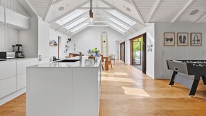A spacious kitchen with a central island, a dining area with a wooden table, and a foosball table. - Cozy home in Vejby with sauna (Vejby)