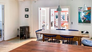 A dining area with a wooden table and blue chairs, a black stove, and a white brick wall with framed pictures. - 4 bedroom awesome home in Vejby (Vejby)
