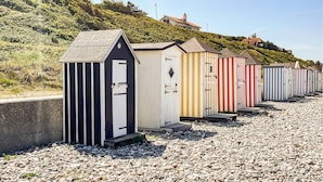 A row of beach huts with sloped roofs, arranged on a pebbled beach with a hillside in the background. - 4 bedroom awesome home in Vejby (Vejby)