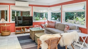 A sunroom with a TV, sofa, wicker furniture, and large windows. - 4 bedroom awesome home in Vejby (Vejby)