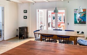 A dining area with a wooden table and blue chairs, a black stove, and a white brick wall with framed pictures.