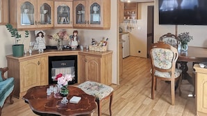 A living room with wooden cabinets, a television, a dining table with floral chairs, and a small refrigerator. - Cozy home in Stankowice with sauna (Stankowice)