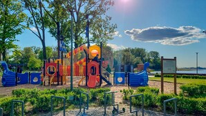 A playground with slides and climbing structures, surrounded by greenery and a clear sky.
