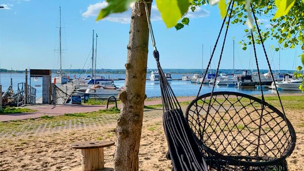 A hammock chair on a sandy beach with a view of boats in the background.