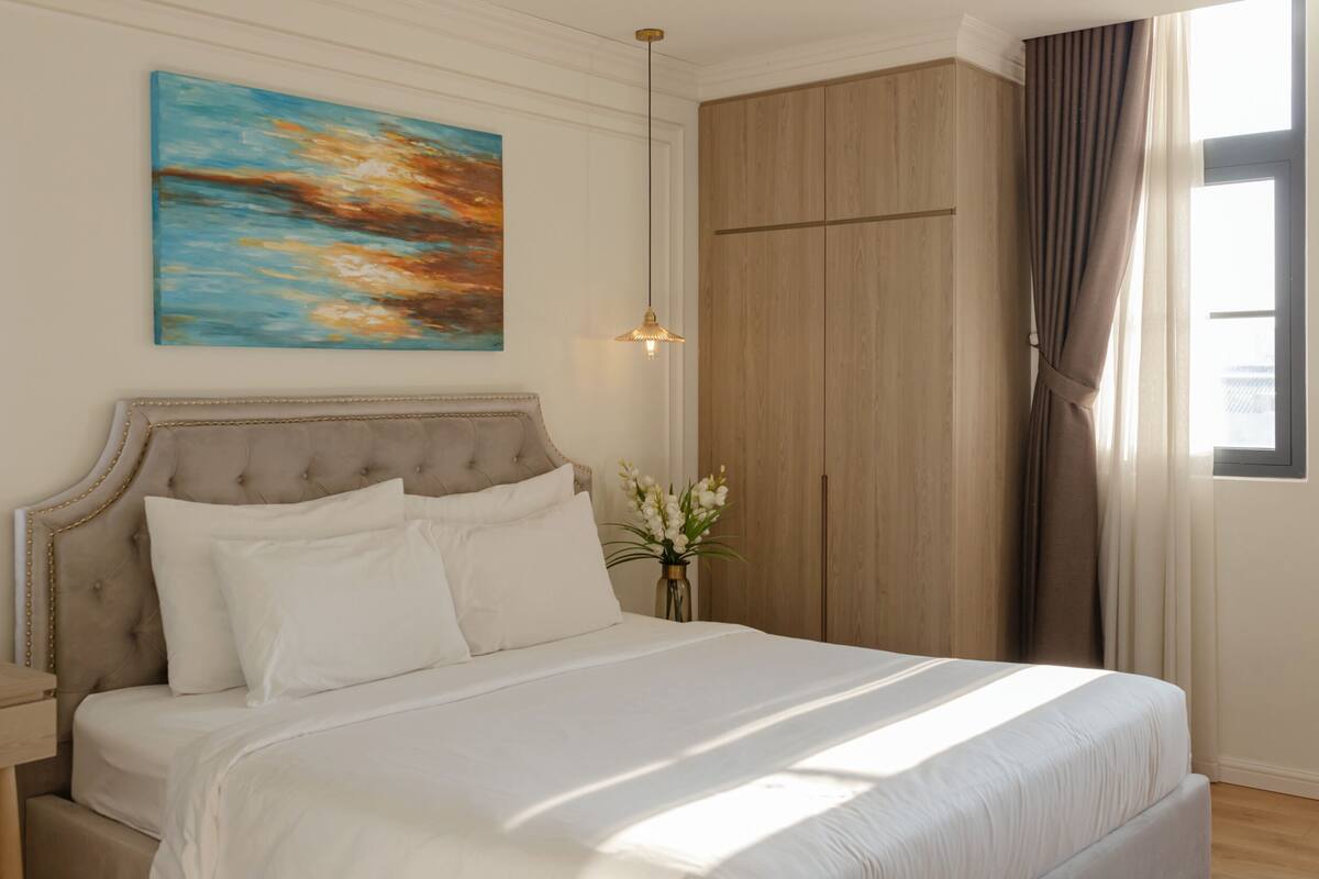 A neatly made bed with white linens, a tufted headboard, and a bedside table with a lamp.