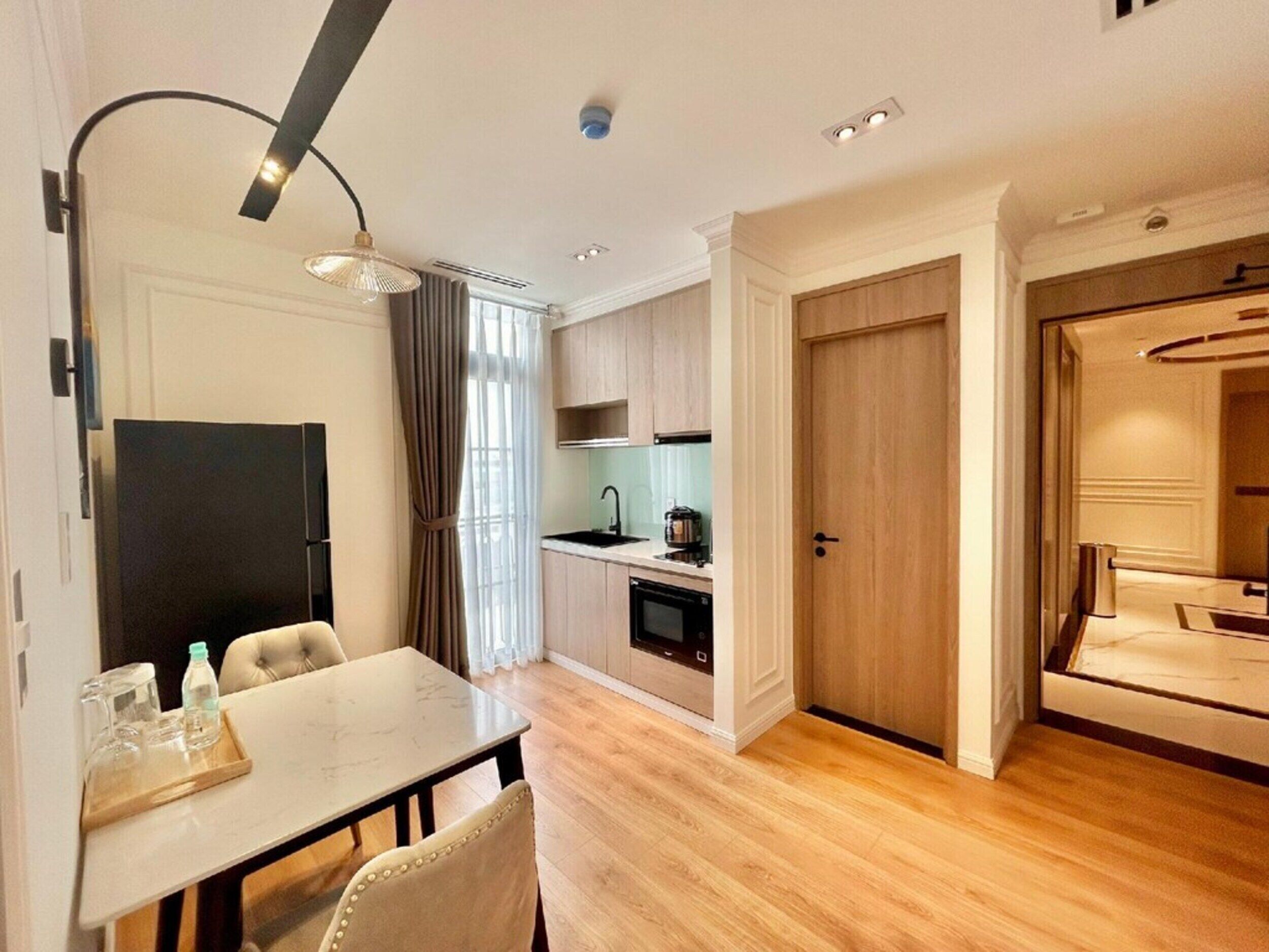 A modern hotel room with a dining area, kitchenette, and a separate bedroom.