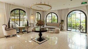 A spacious lobby with a round table, two armchairs, a sofa, and large arched windows with a view of greenery. - S Home Apartment by DDH (Ho Chi Minh City)