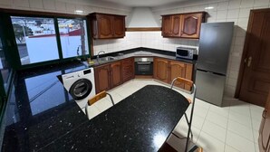 A compact kitchen with wooden cabinets, a stainless steel refrigerator, a washing machine, and a microwave.
