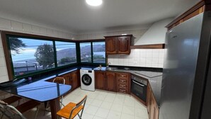 A compact kitchen with a dining area, a washing machine, and a large window offering a view.