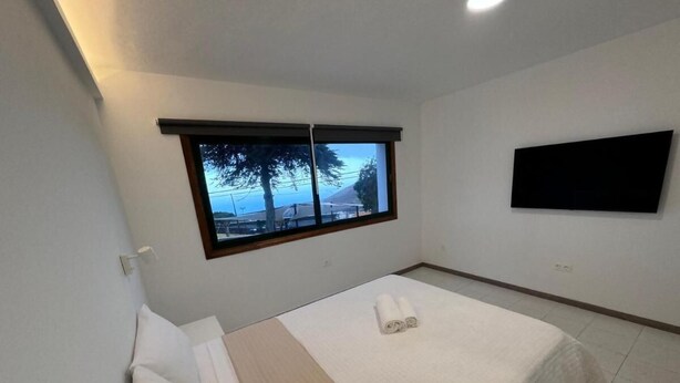 A small, clean room with a bed, a window with a view, and a flat-screen TV on the wall.