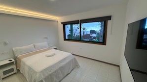 A modern bedroom with a large bed, a nightstand, a TV, and a window with a city view.