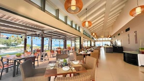 A spacious outdoor dining area with multiple tables and chairs, large windows offering views of the ocean, and hanging wicker lamps. - BIG SALE | Full equipment apartment | Pool & beach (Đà Nẵng)