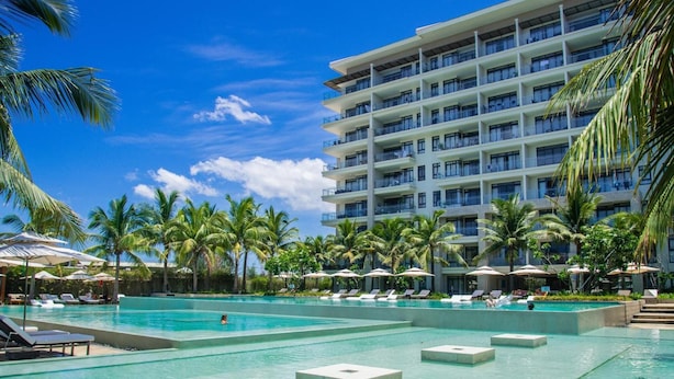 A hotel with a large pool area, multiple balconies, and palm trees. - BIG SALE | Full equipment apartment | Pool & beach (Đà Nẵng)