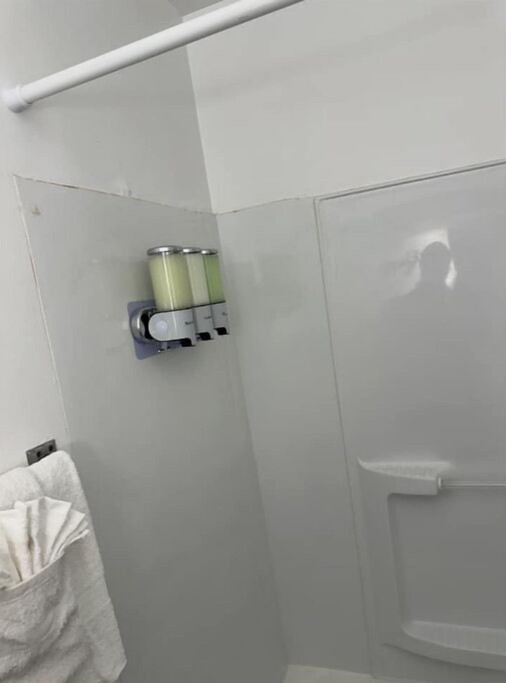 A bathroom with a towel rack, a soap dispenser, and a shower stall.