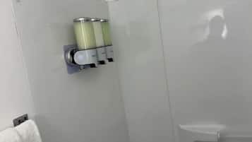 A bathroom with a towel rack, a soap dispenser, and a shower stall.