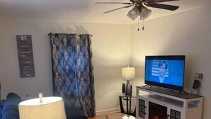Un salon équipé d’un ventilateur de plafond, d’une télévision, d’un canapé, d’une table basse et d’une cheminée.