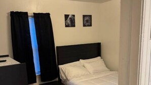 Une chambre à coucher avec un lit, un bureau et une chaise. Deux tableaux encadrés sont accrochés au mur.