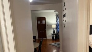 Un couloir étroit, doté d’un plancher en bois, mène à une salle à manger où se trouvent une table et des chaises.