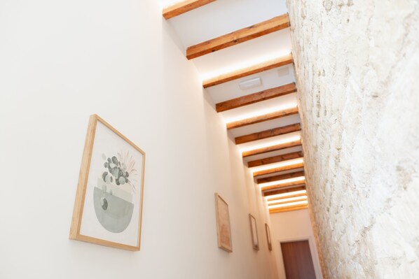 Una escalera con vigas de madera y una pared blanca decorada con obras enmarcadas.