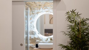 A bathroom with a stone wall, a wooden vanity, a white sink, and a mirror.