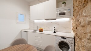 A compact kitchen with white cabinets, a microwave, a washing machine, and a small window.