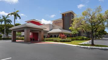 A hotel entrance with a covered waiting area, a red building, and a parking lot.