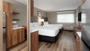Habitación de hotel con dos camas, un escritorio, televisión, ventana y kitchenette.