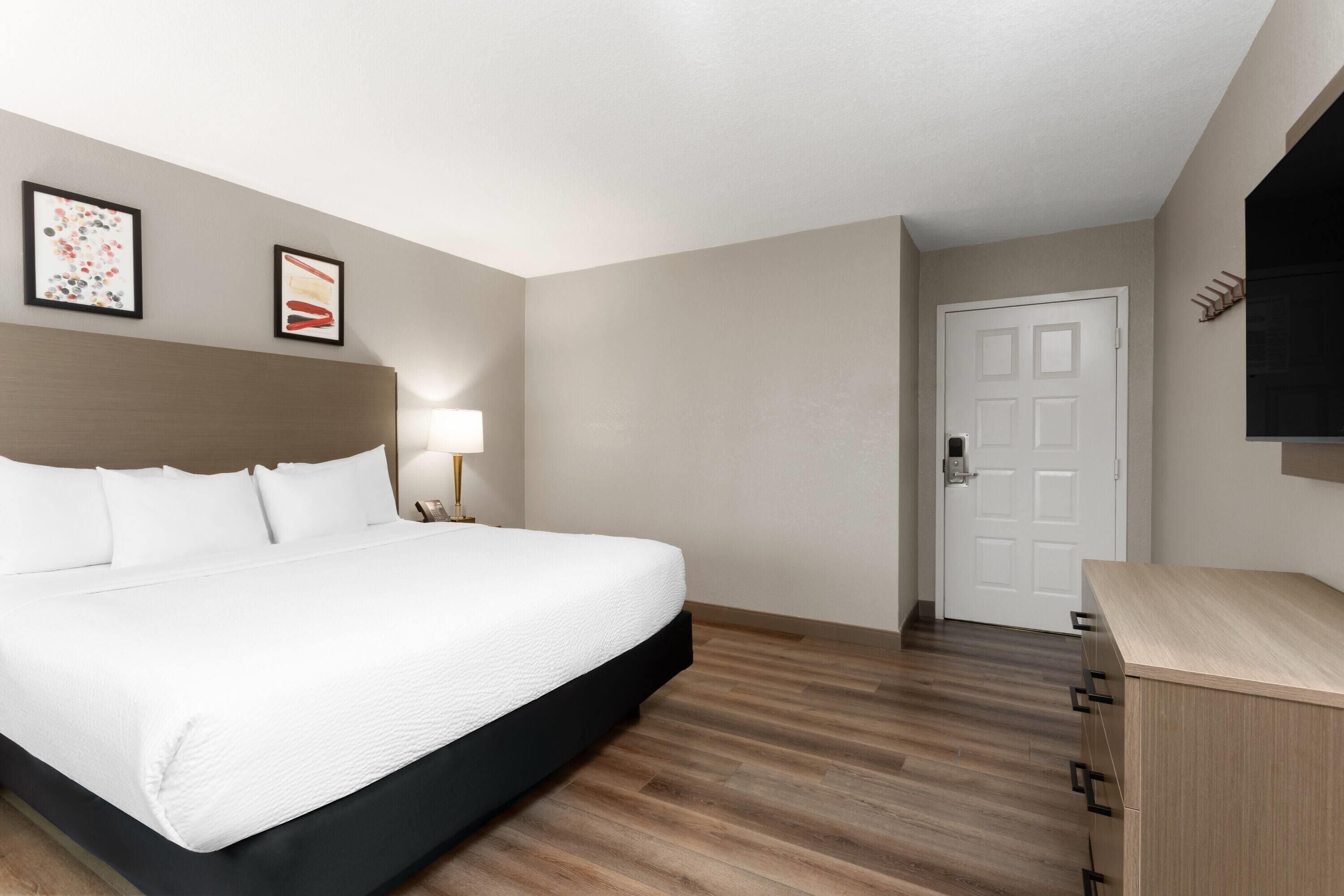 Une chambre d’hôtel avec un grand lit, une lampe de chevet, une commode en bois et deux tableaux encadrés au mur.