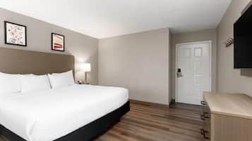 Une chambre d’hôtel avec un grand lit, une lampe de chevet, une commode en bois et deux tableaux encadrés au mur.