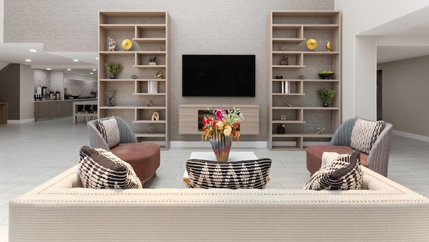 Amplia sala de estar con un televisor de pantalla plana, dos sofás con cojines estampados y un jarrón decorativo con flores sobre una mesa de centro.