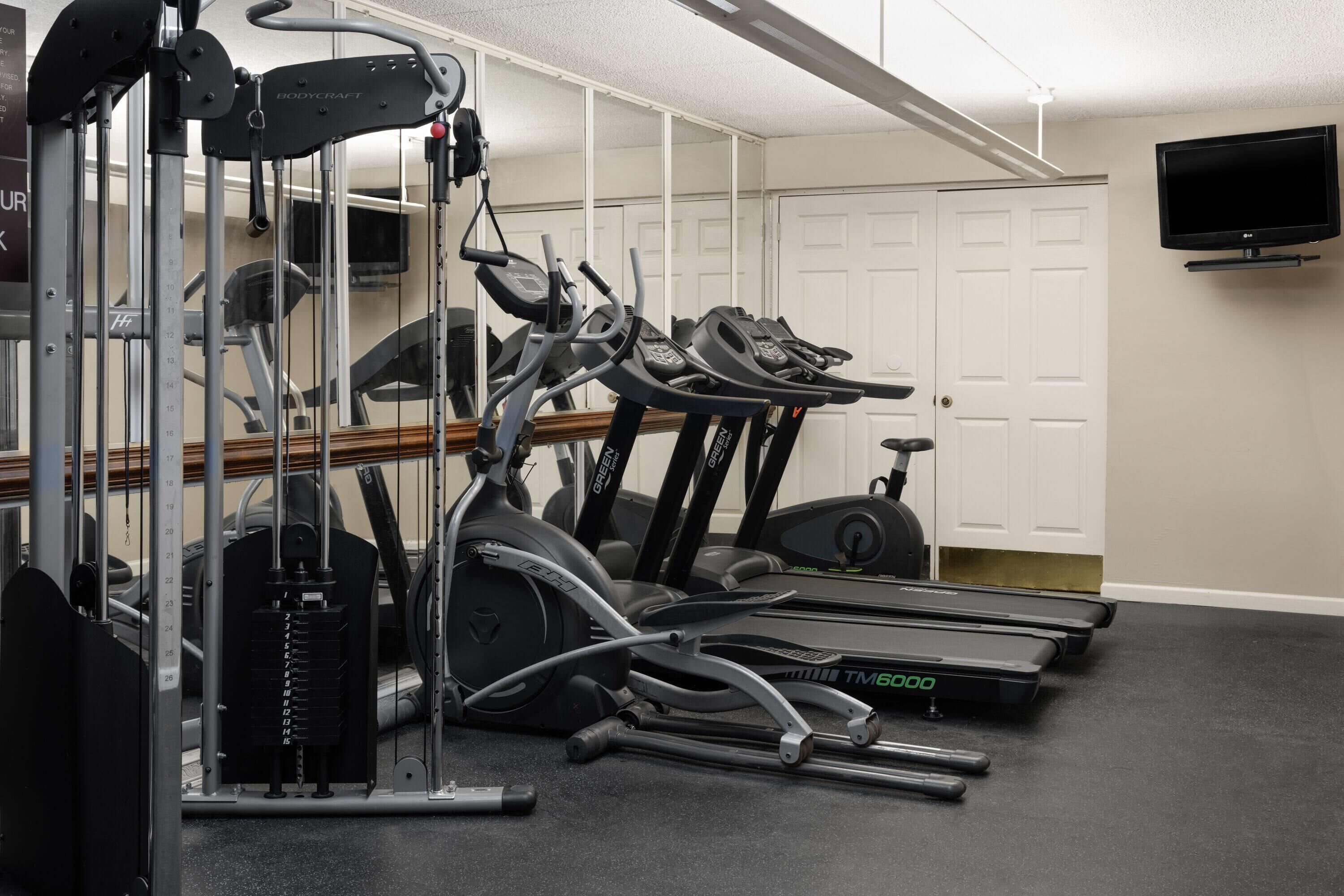 Un gimnasio con cintas de correr, máquinas de pesas y un televisor montado en la pared.