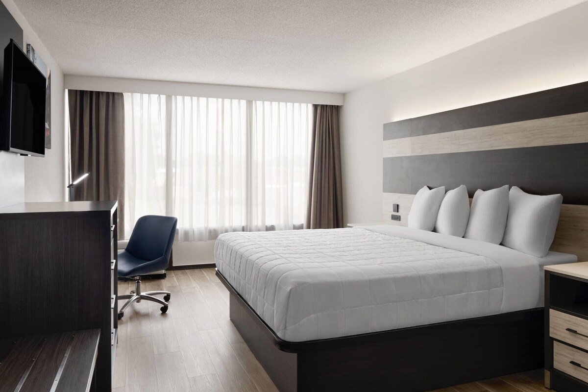 A modern hotel room with a large bed, a desk, a chair, and a TV mounted on the wall.