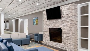 A modern living room with a stone fireplace, grey sofas, and a flat-screen TV mounted on the wall. - Baymont By Wyndham Williamsburg I-64 (Williamsburg)