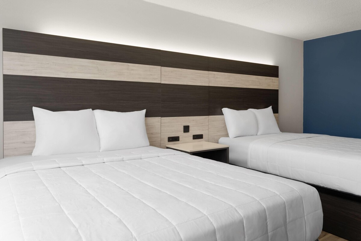 A hotel room with two beds, a wooden headboard, a small bedside table, and a blue accent wall.
