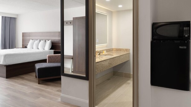 A hotel room with a bed, a small seating area, a bathroom with a sink and mirror, and a microwave. - Baymont By Wyndham Williamsburg I-64 (Williamsburg)