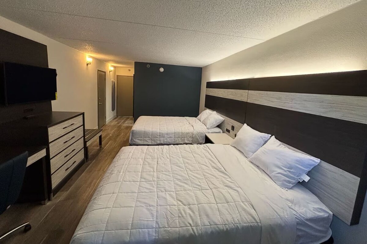 A hotel room with two beds, a desk, and a television.