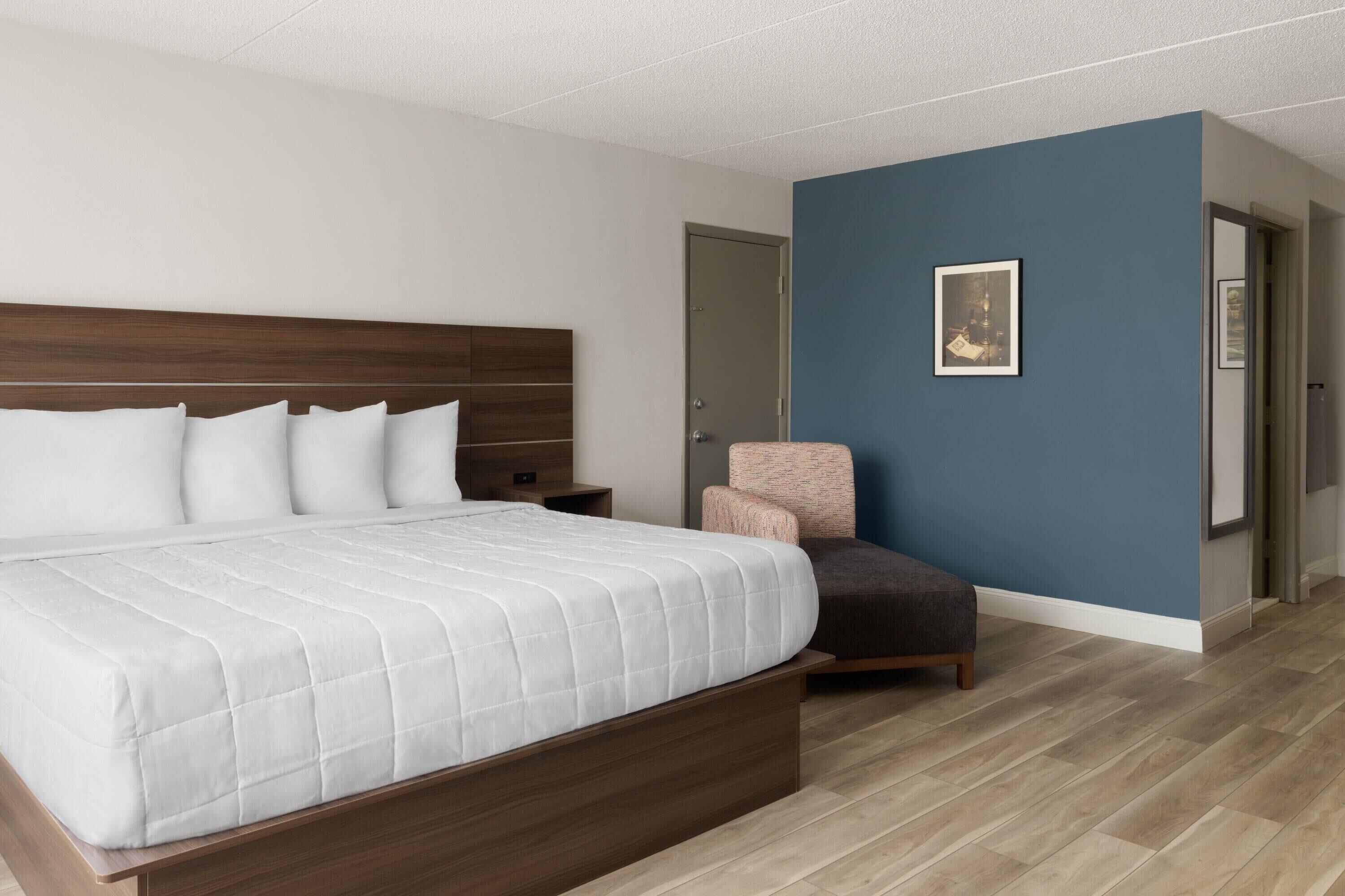 A modern bedroom with a large bed, a wooden headboard, a blue accent wall, and a framed picture.