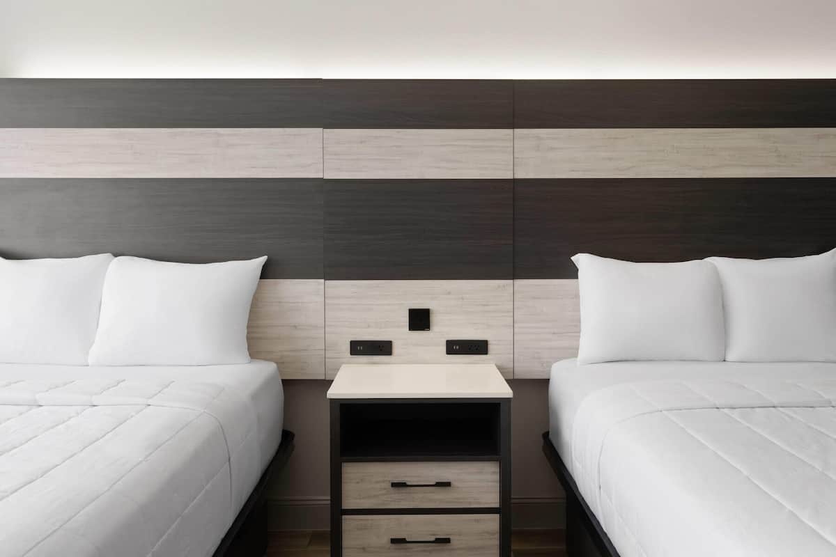 A hotel room with two beds, a nightstand with drawers, and a modern headboard.