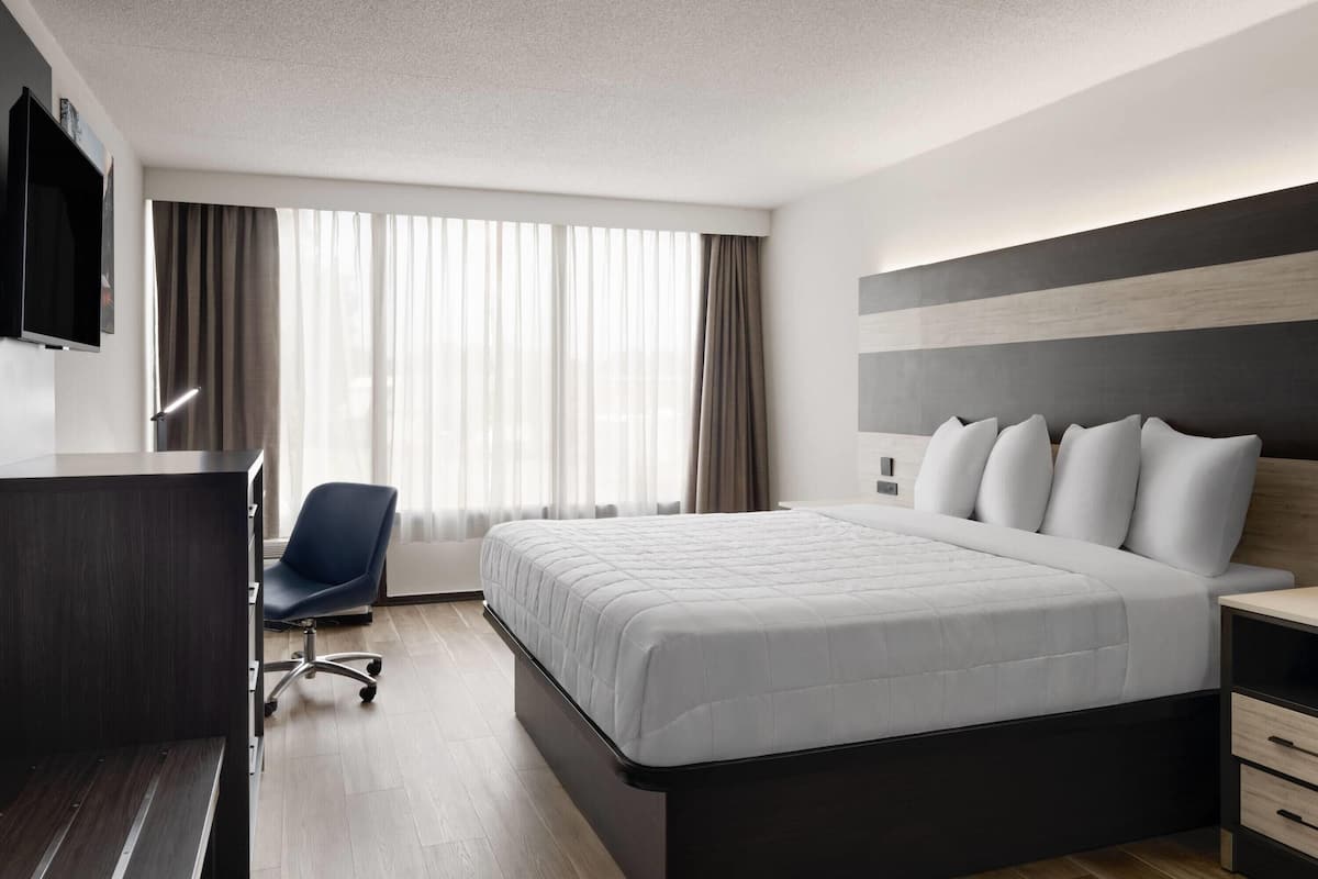 A modern hotel room with a large bed, a desk, a chair, and a TV mounted on the wall.