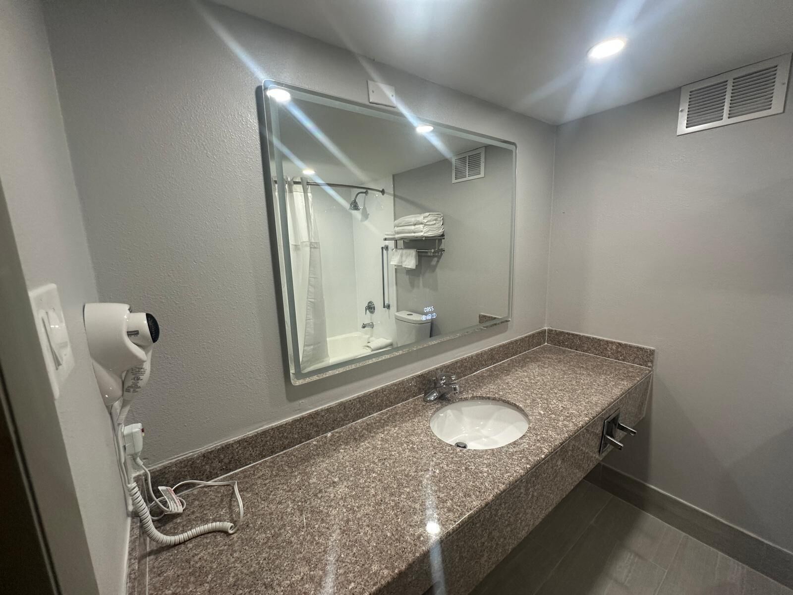 A modern bathroom with a granite countertop, a sink, a mirror, and a shower area.