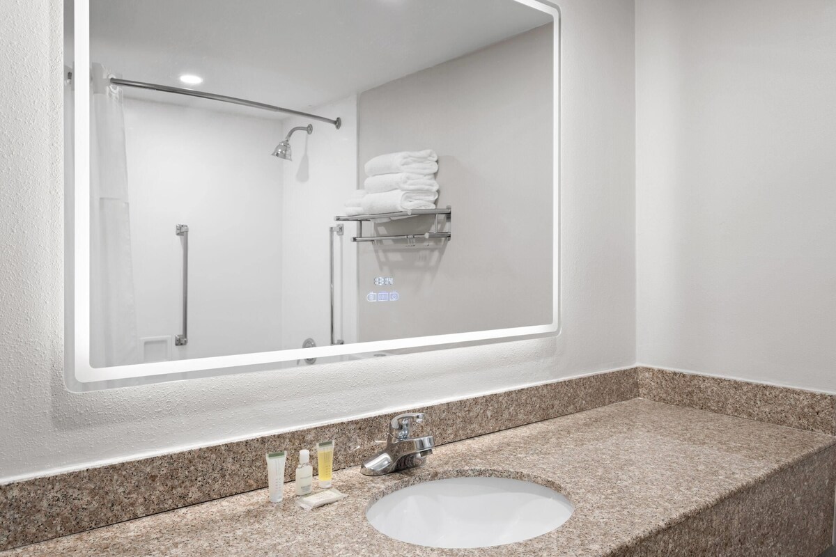 A bathroom with a large mirror, a granite countertop, a sink, and a towel rack with folded towels.