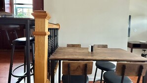 Een eetgedeelte met een houten tafel en zwarte stoelen, een houten kolom en een uitzicht op de keuken achterin.
