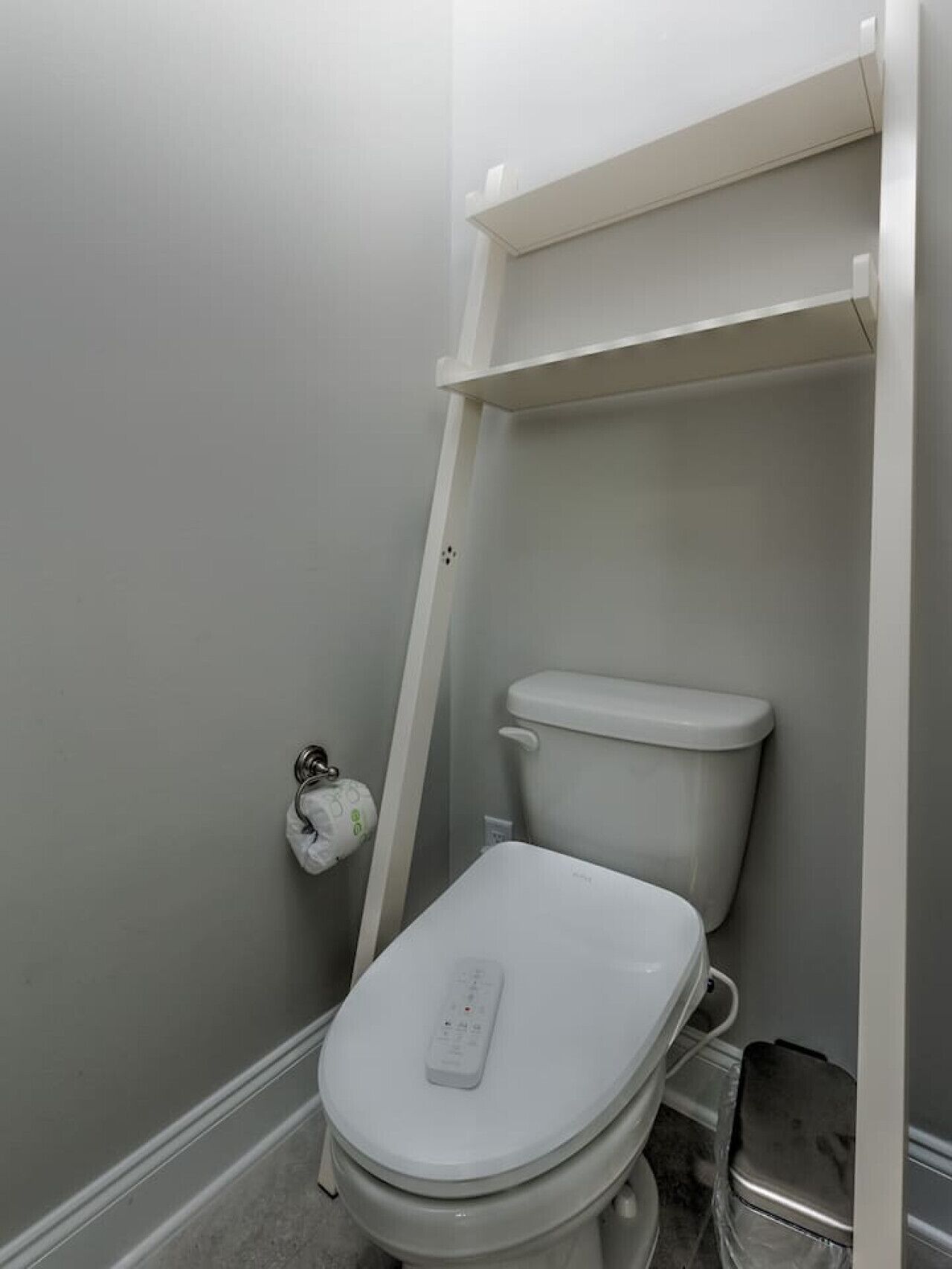 A small, modern bathroom with a white toilet, a toilet paper holder, and a trash bin.