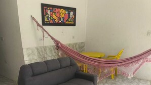 A living room with a gray sofa, a small black table, a hammock, and a colorful painting on the wall. - Renata Fogaça  (Maragogi)