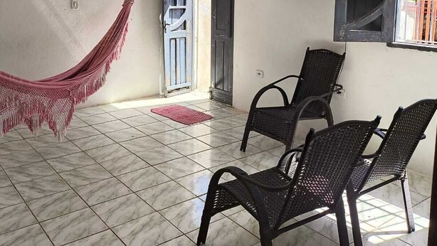 A room with a hammock, two chairs, a window with bars, and a door leading outside. - Renata Fogaça  (Maragogi)