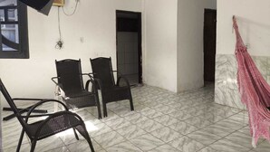 A room with two wicker chairs, a television, a pink hammock, and a tiled floor. - Renata Fogaça  (Maragogi)