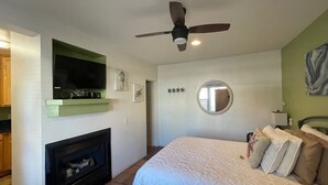 A bedroom with a bed, a ceiling fan, a fireplace, a television, and artwork on the walls. - BESO DEL SOL (Huntington Beach)