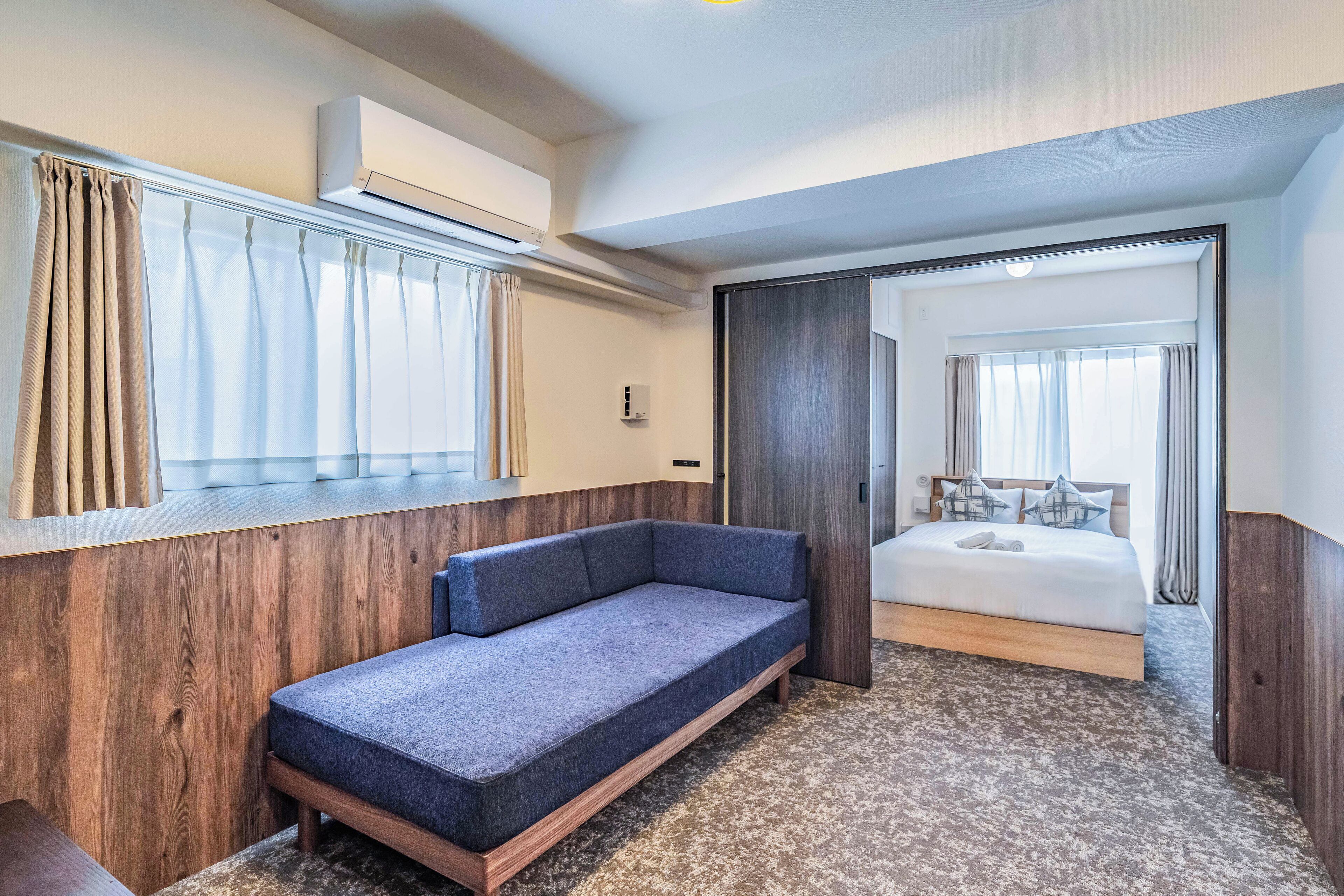 A modern hotel room with a sofa, a bed, and an air conditioning unit.